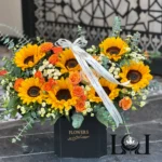 باکس گل کلاهدار BL156 شامل آفتابگردان، رز مینیاتوری و اوکا – ابعاد عرض ۶۰ ارتفاع ۶۰ سانتی‌متر – گل فروشی لونا فلاور کرج